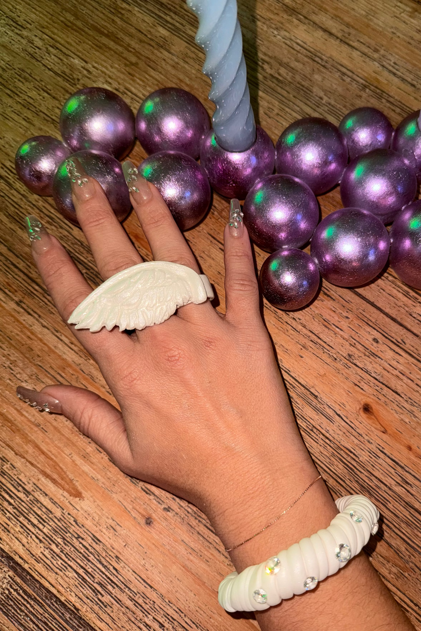Hand wearing a white angel wing ring colorful beads on a wooden surface